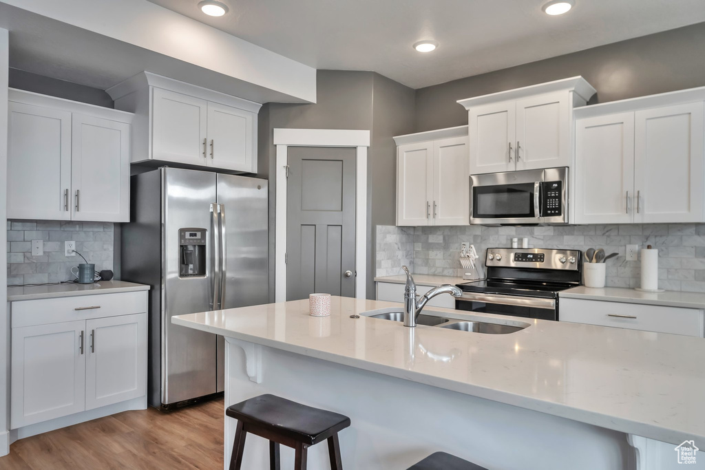 Kitchen featuring stainless steel appliances, white cabinetry, light hardwood / wood-style floors, and a kitchen bar