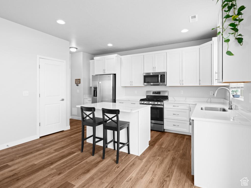 Kitchen with white cabinetry, a center island, sink, wood-type flooring, and appliances with stainless steel finishes