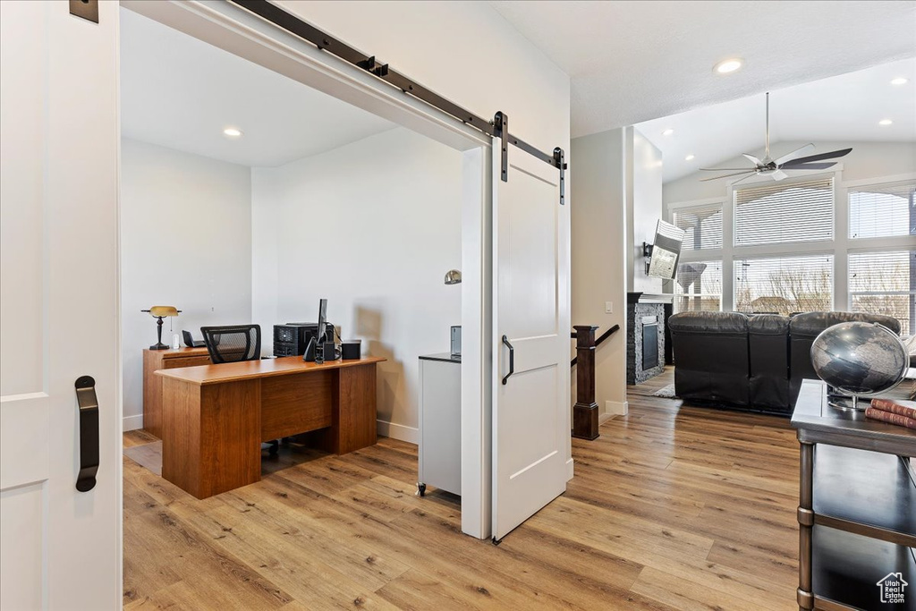 Home office featuring a barn door, lofted ceiling, light hardwood / wood-style flooring, and ceiling fan