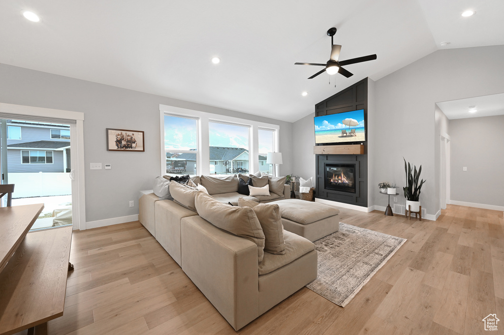 Living room featuring a large fireplace, light hardwood / wood-style flooring, lofted ceiling, and ceiling fan