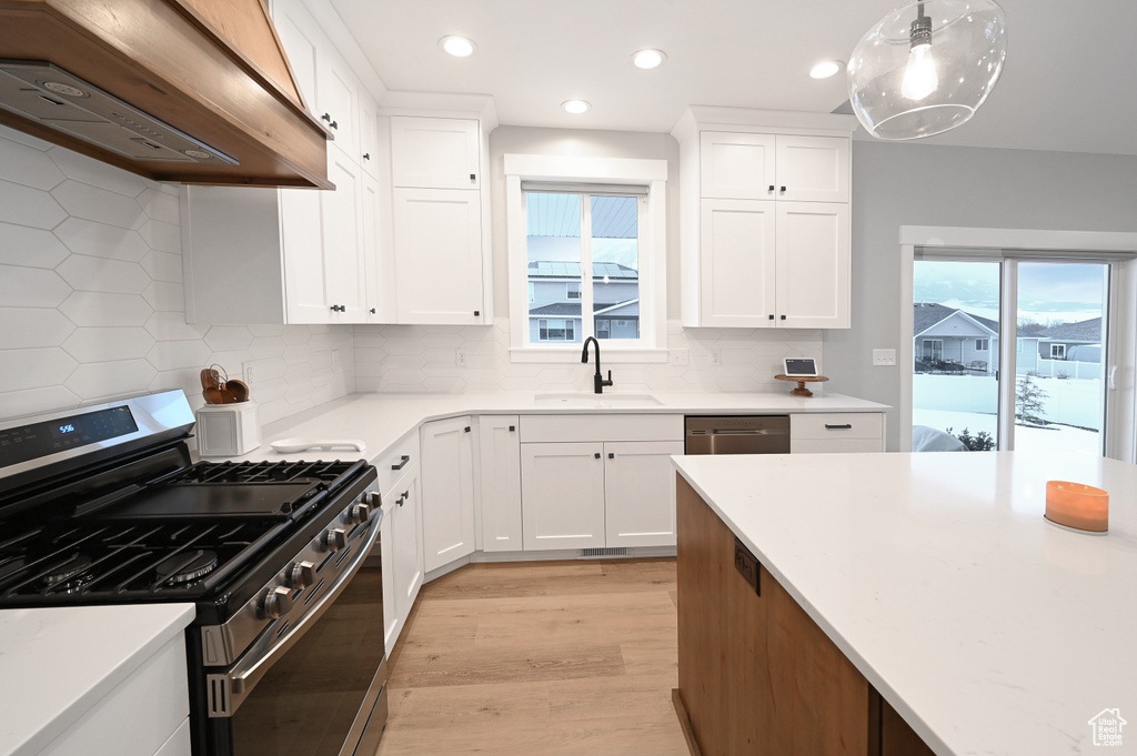 Kitchen featuring backsplash, stainless steel appliances, custom range hood, and light hardwood / wood-style flooring