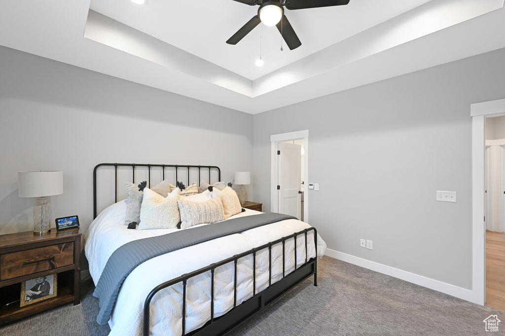 Bedroom featuring a tray ceiling, dark carpet, and ceiling fan