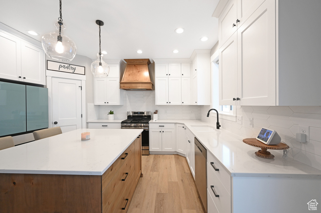 Kitchen featuring custom range hood, sink, decorative light fixtures, light wood-type flooring, and stainless steel appliances