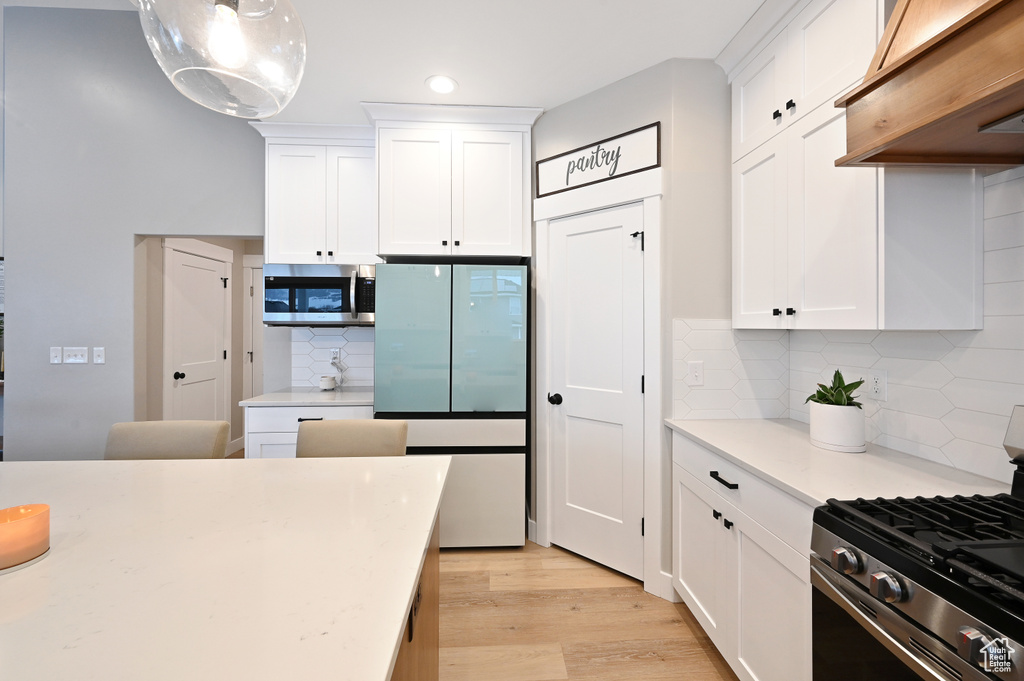 Kitchen with tasteful backsplash, appliances with stainless steel finishes, light hardwood / wood-style floors, hanging light fixtures, and white cabinets