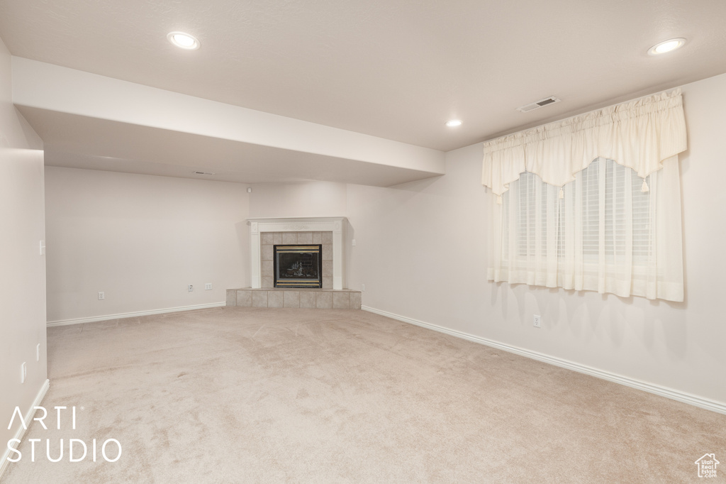 Unfurnished living room featuring a tile fireplace and light carpet