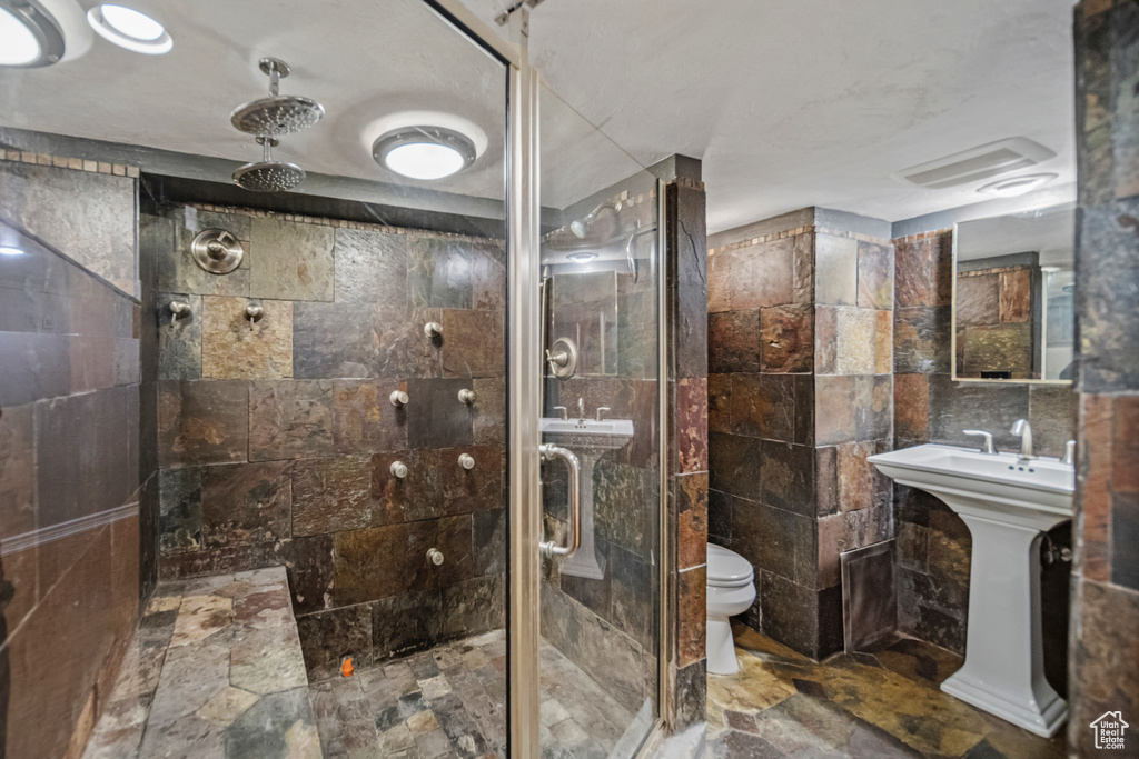 Bathroom with tile flooring, tile walls, toilet, and a shower with shower door