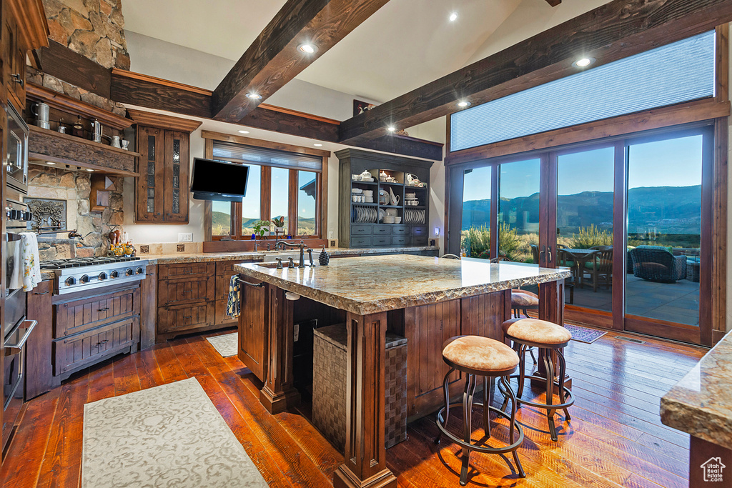 Kitchen with dark hardwood / wood-style flooring, an island with sink, a mountain view, a kitchen bar, and light stone counters