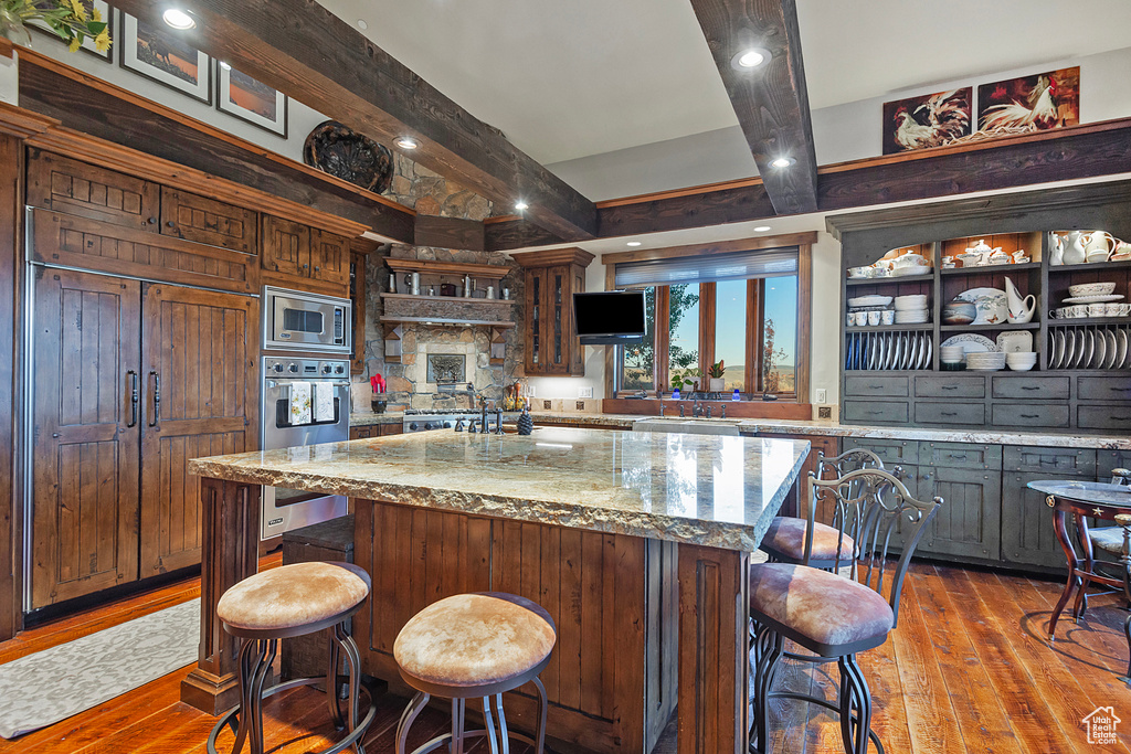 Kitchen with a kitchen island, built in appliances, a kitchen bar, and wood-type flooring