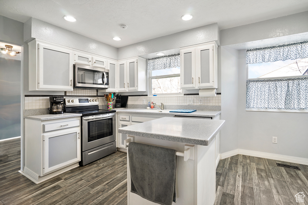 Kitchen with backsplash, stainless steel appliances, white cabinetry, and dark hardwood / wood-style floors