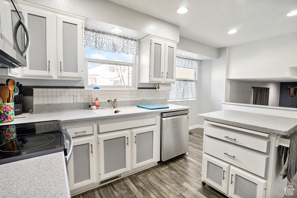 Kitchen with dark hardwood / wood-style flooring, sink, backsplash, white cabinets, and stainless steel appliances