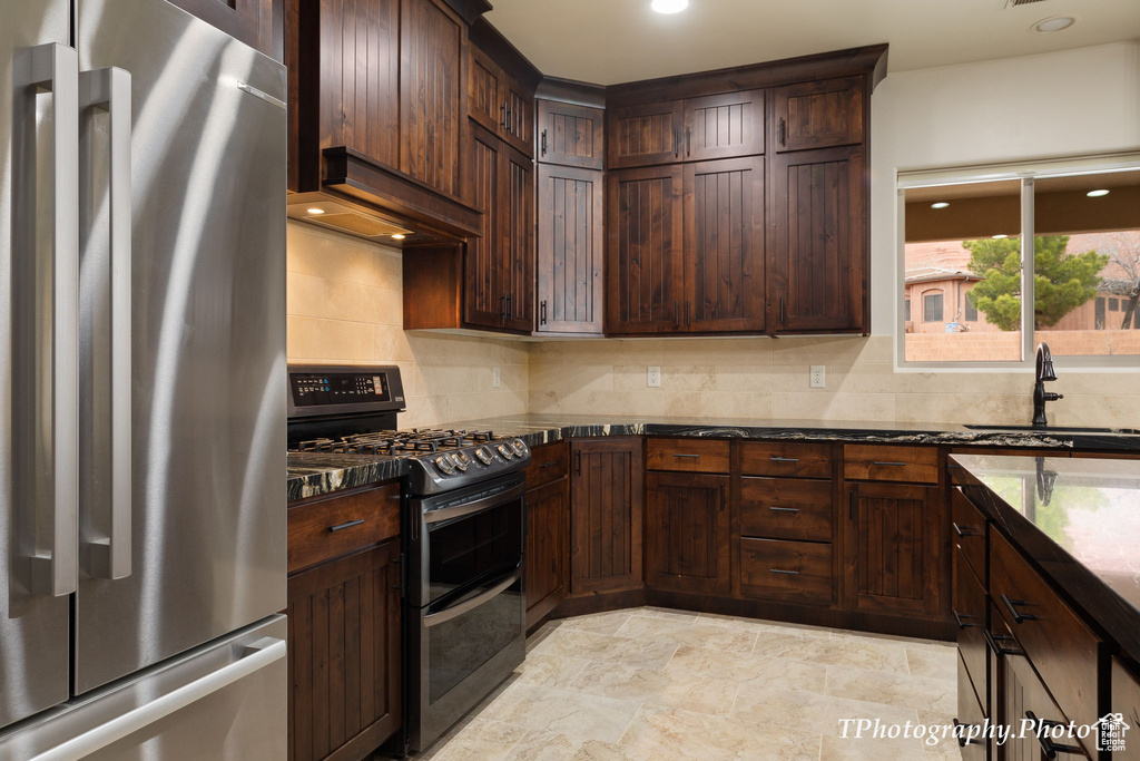 Kitchen with backsplash, appliances with stainless steel finishes, light tile floors, dark stone counters, and sink