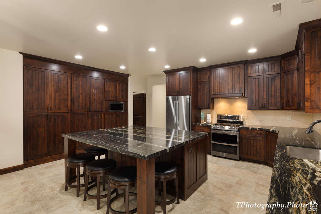 Kitchen featuring dark stone countertops, appliances with stainless steel finishes, sink, a center island, and a kitchen bar