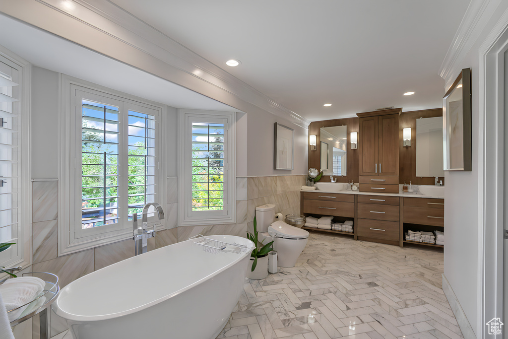 Bathroom featuring tile walls, dual bowl vanity, crown molding, a bathtub, and toilet