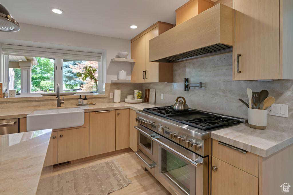 Kitchen featuring sink, tasteful backsplash, wall chimney exhaust hood, light wood-type flooring, and range with two ovens