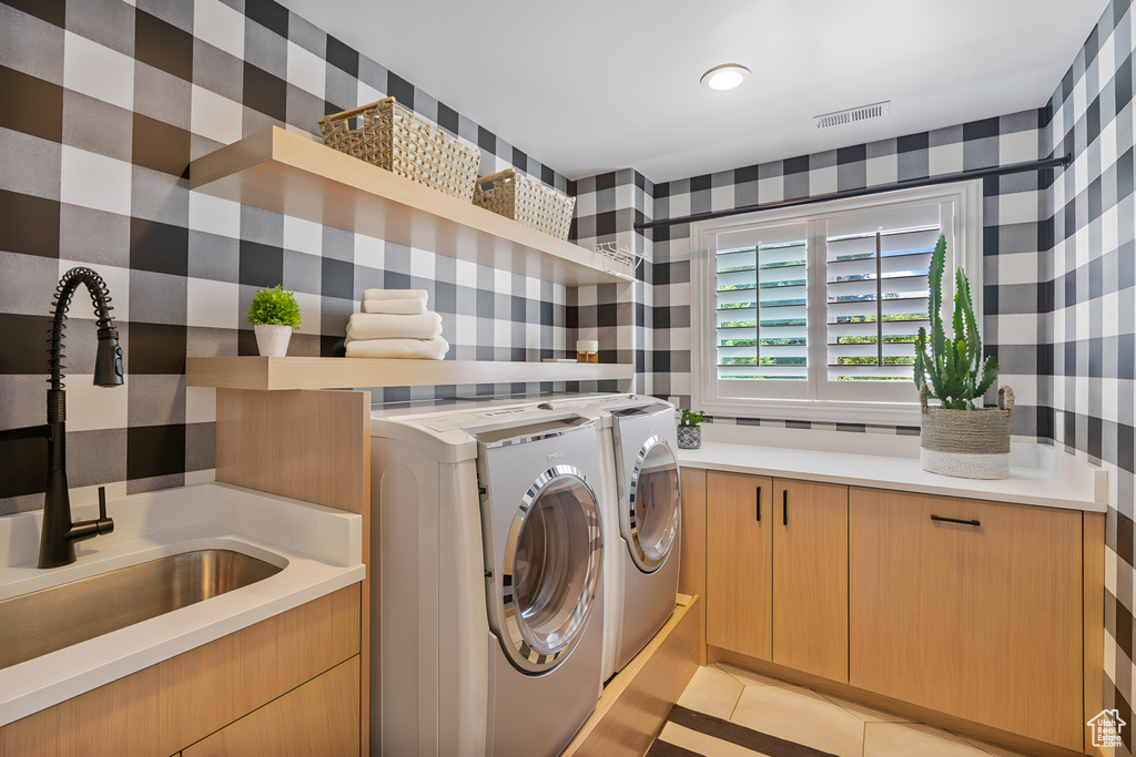 Clothes washing area featuring light tile floors, sink, cabinets, and washer and clothes dryer