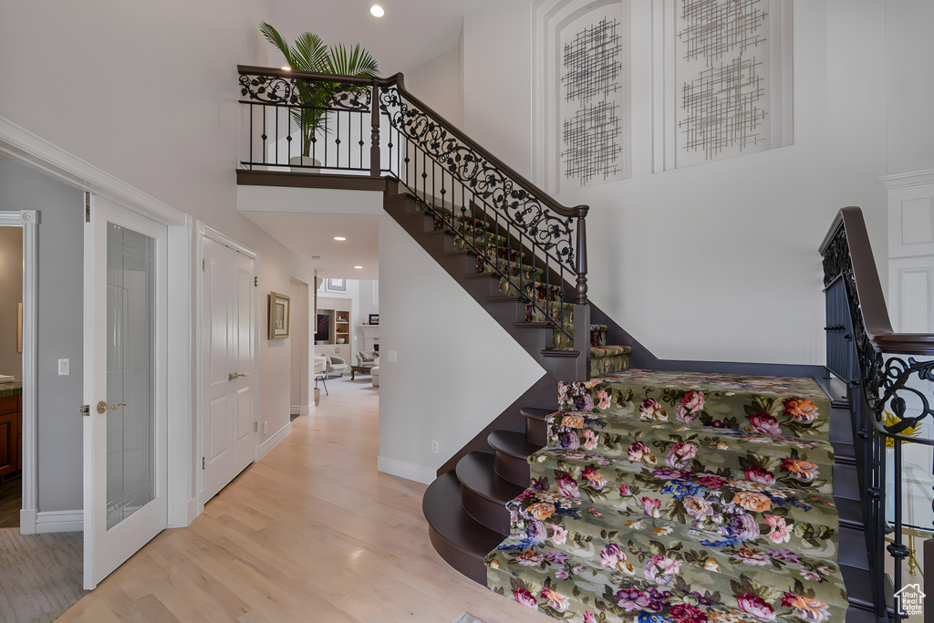 Staircase featuring light hardwood / wood-style flooring, french doors, and a high ceiling