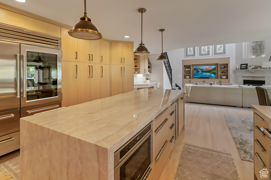 Kitchen with a kitchen island, light wood-type flooring, light brown cabinets, and hanging light fixtures