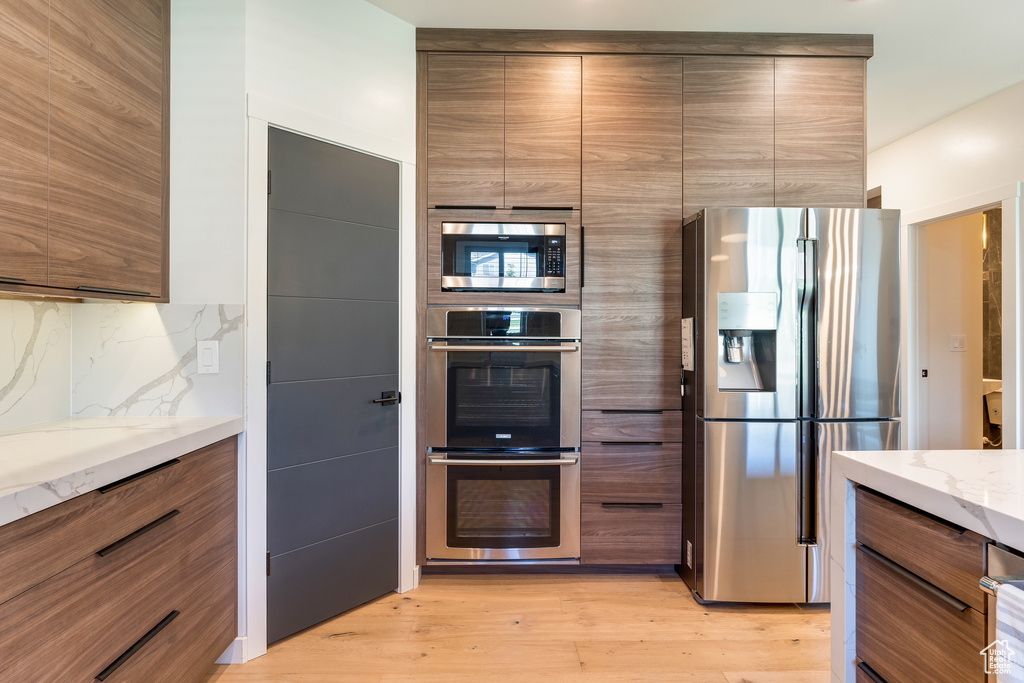 Kitchen featuring stainless steel appliances, light hardwood / wood-style floors, light stone countertops, and backsplash