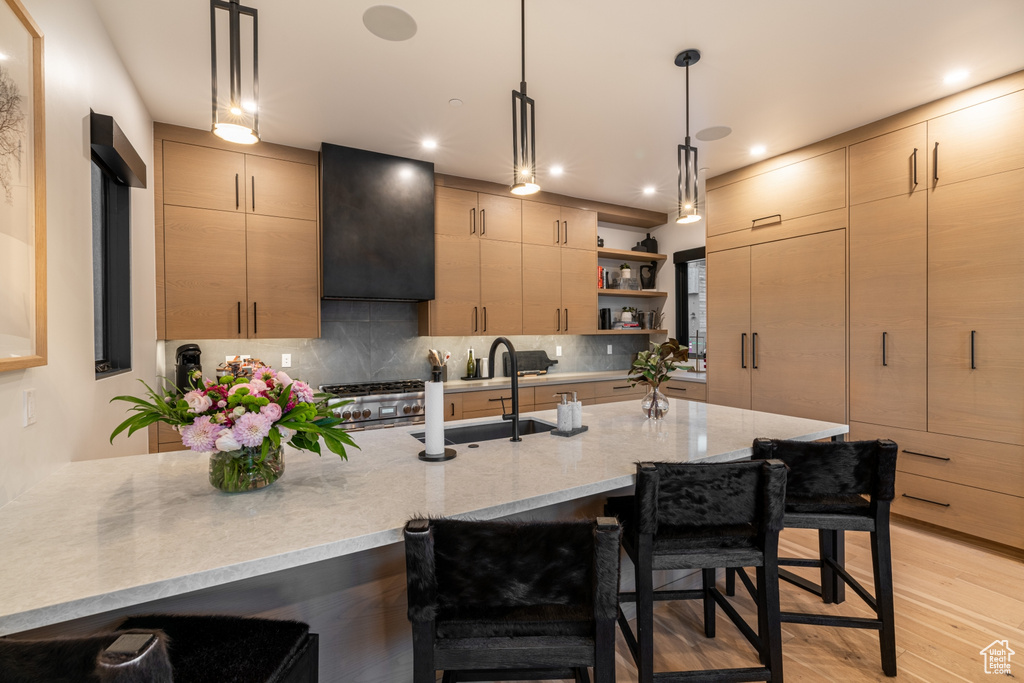 Kitchen featuring light brown cabinets, decorative light fixtures, a breakfast bar area, and light wood-type flooring