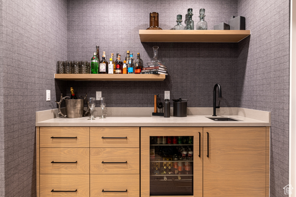 Bar featuring brick wall, beverage cooler, light brown cabinetry, and sink