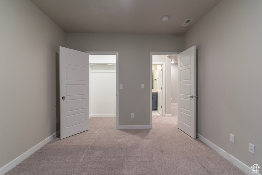 Unfurnished bedroom featuring light colored carpet, a spacious closet, and a closet