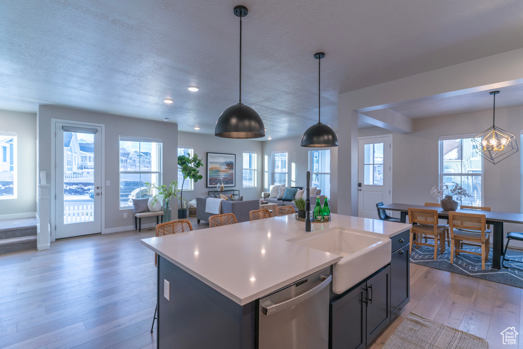 Kitchen with a center island, pendant lighting, stainless steel dishwasher, an inviting chandelier, and light wood-type flooring