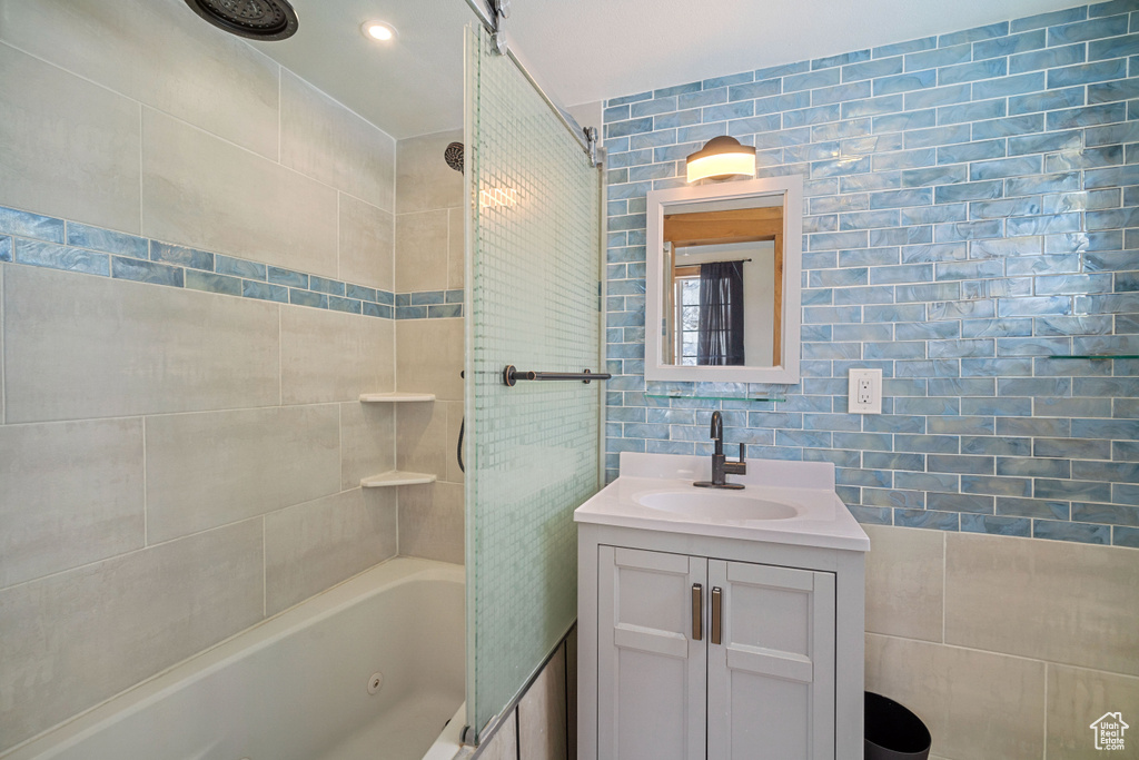 Bathroom featuring tile walls, large vanity, and tiled shower / bath