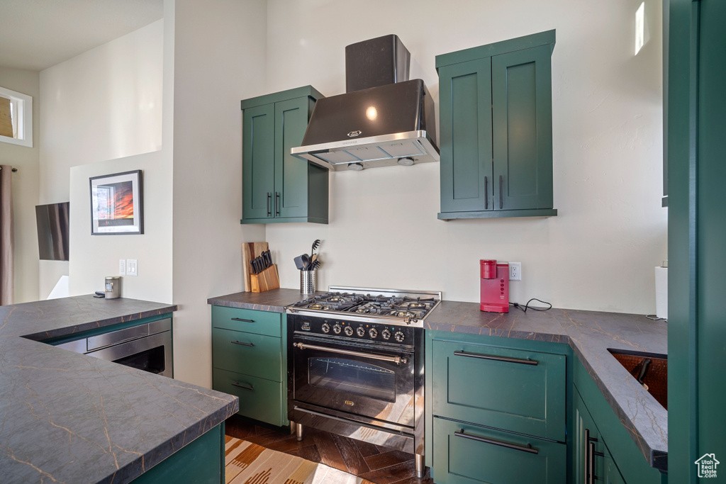 Kitchen featuring wall chimney range hood, double oven range, stainless steel oven, light hardwood / wood-style floors, and green cabinetry
