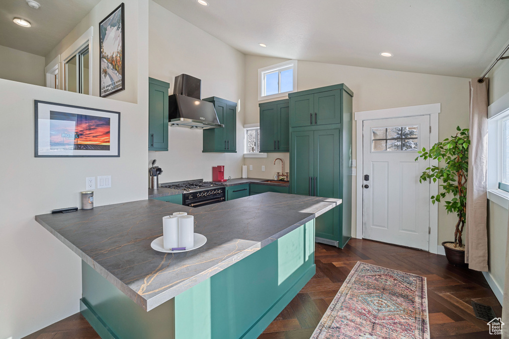 Kitchen featuring kitchen peninsula, range with gas stovetop, dark parquet flooring, and wall chimney range hood