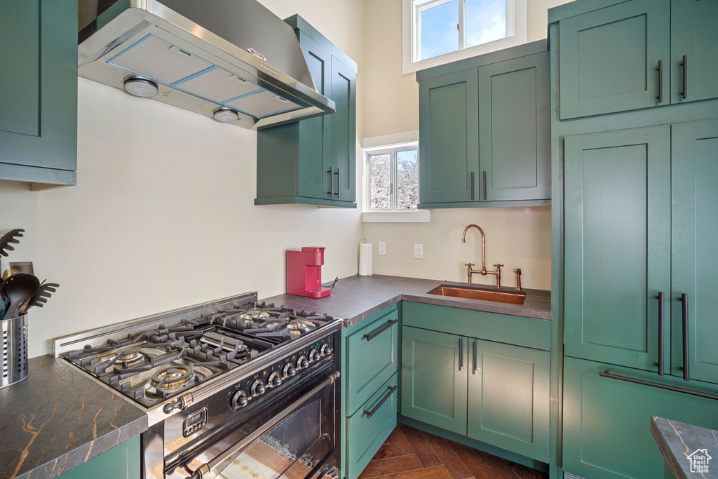 Kitchen with gas range, green cabinetry, sink, dark parquet floors, and wall chimney range hood