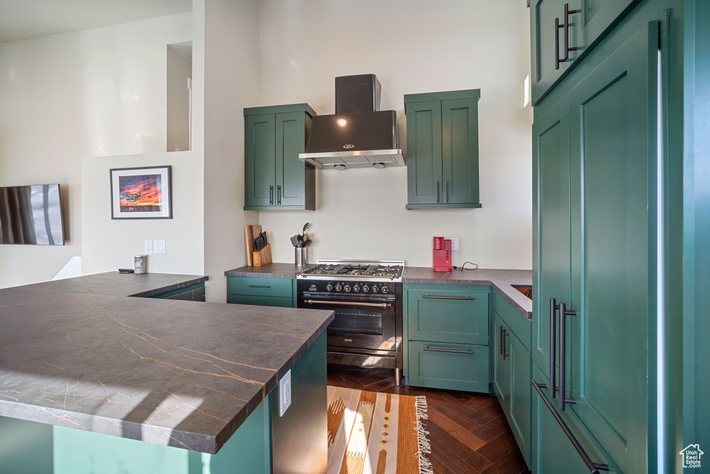 Kitchen with high end appliances, green cabinetry, dark parquet floors, and wall chimney range hood