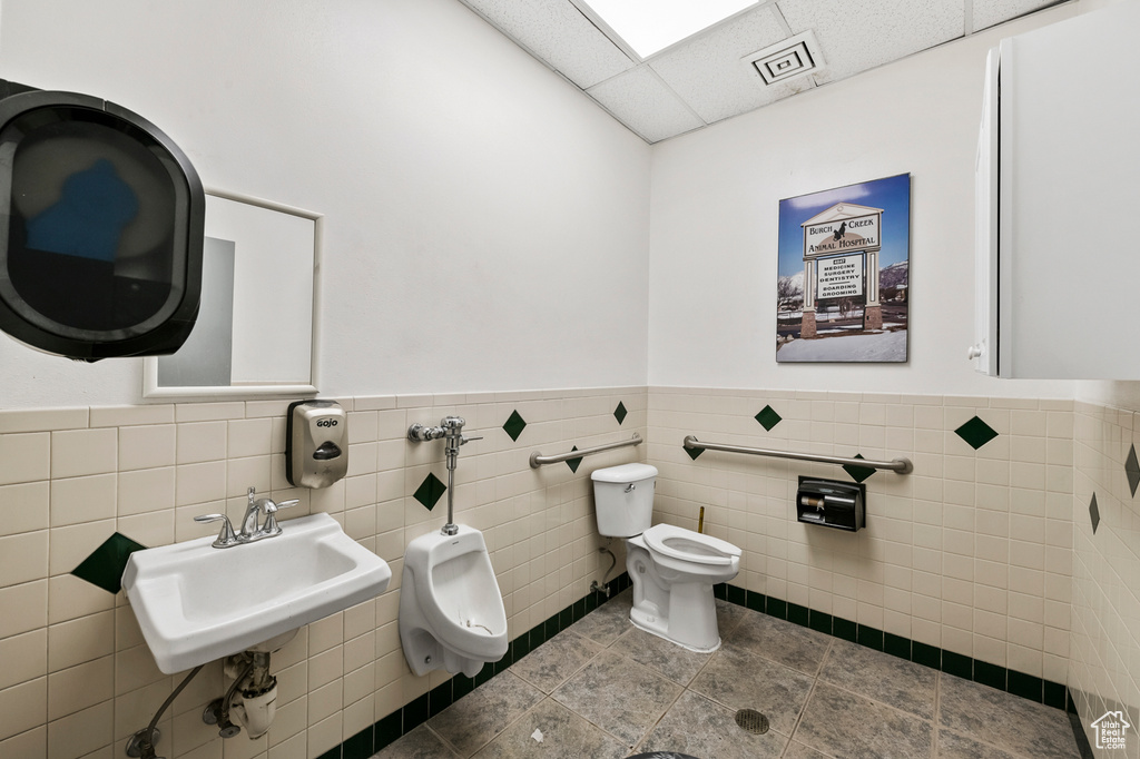Bathroom with a paneled ceiling, tile flooring, toilet, and tile walls