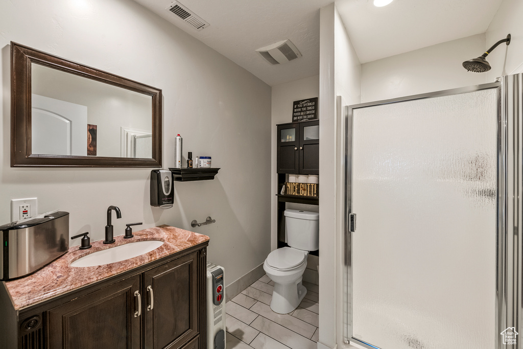 Bathroom with toilet, large vanity, a shower with door, and tile floors