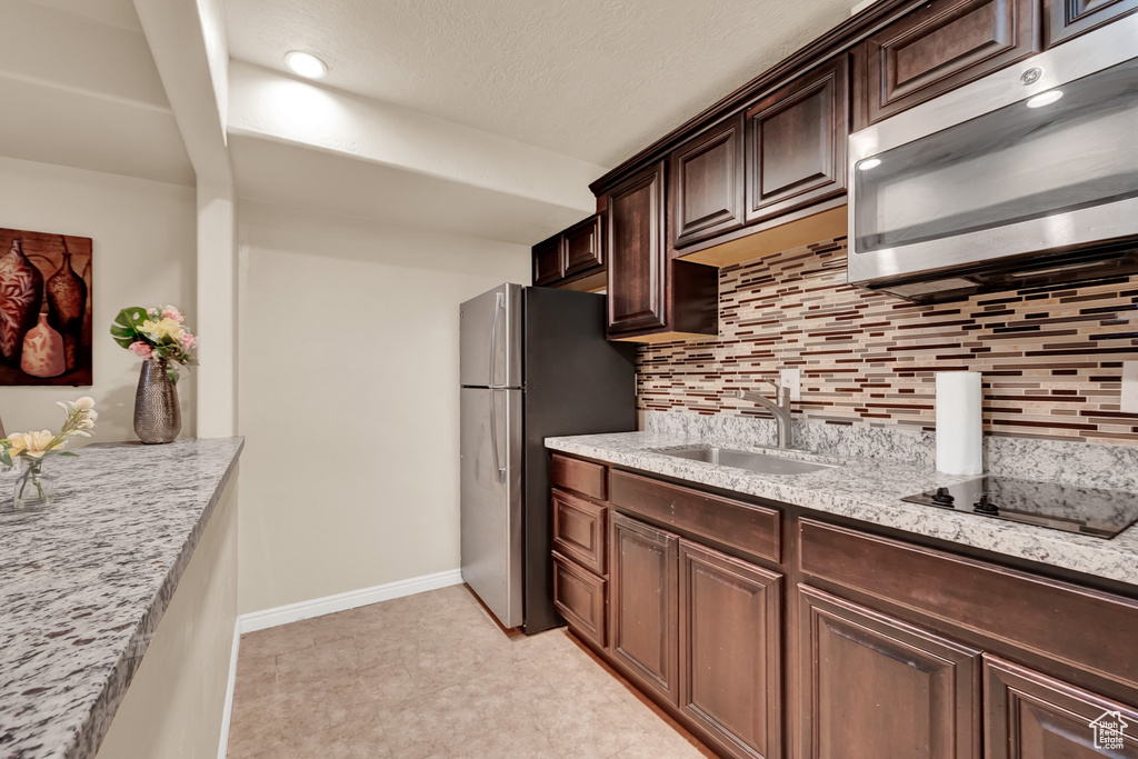 Kitchen featuring tasteful backsplash, light tile floors, stainless steel appliances, sink, and dark brown cabinets