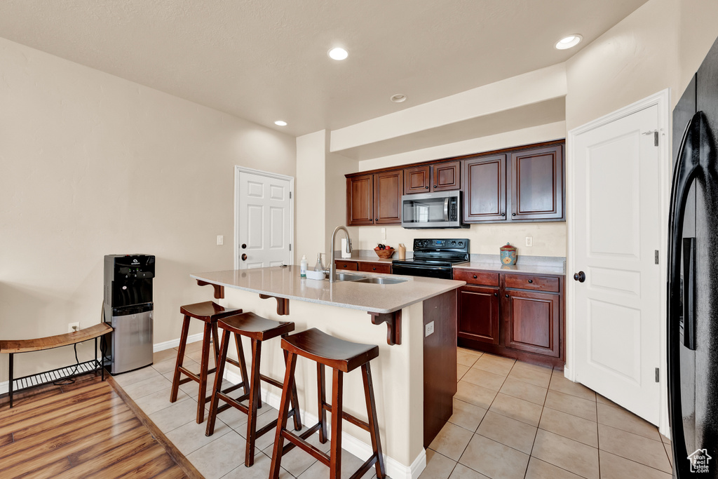 Kitchen featuring light tile flooring, black appliances, sink, a kitchen bar, and a kitchen island with sink