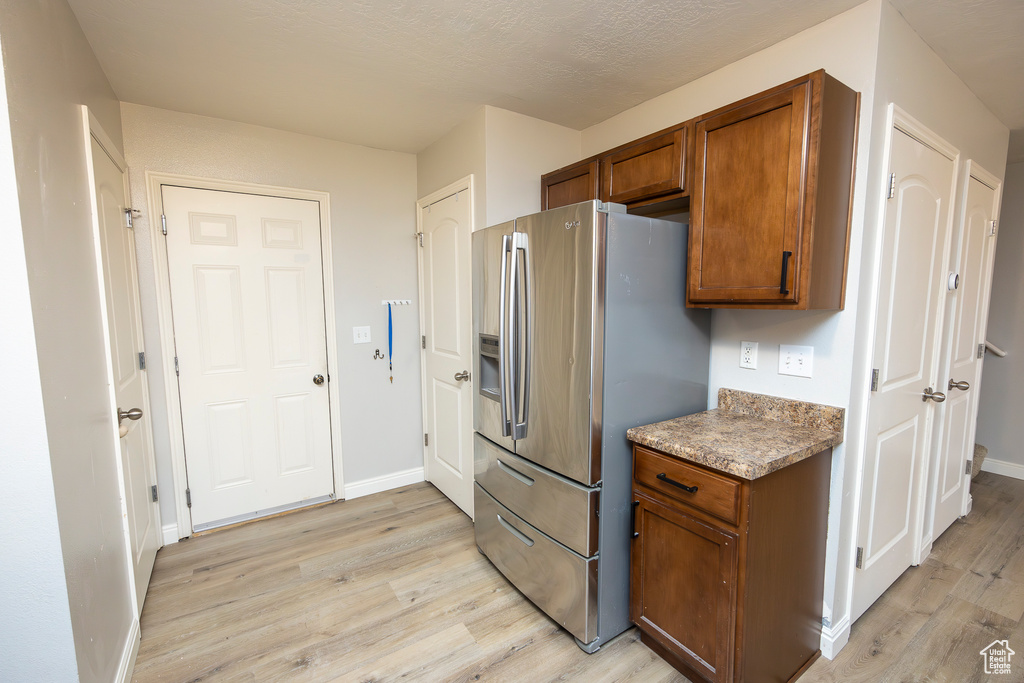 Kitchen featuring stainless steel fridge, light hardwood / wood-style flooring, and light stone counters