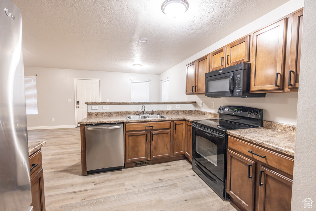 Kitchen featuring kitchen peninsula, sink, black appliances, and light hardwood / wood-style floors