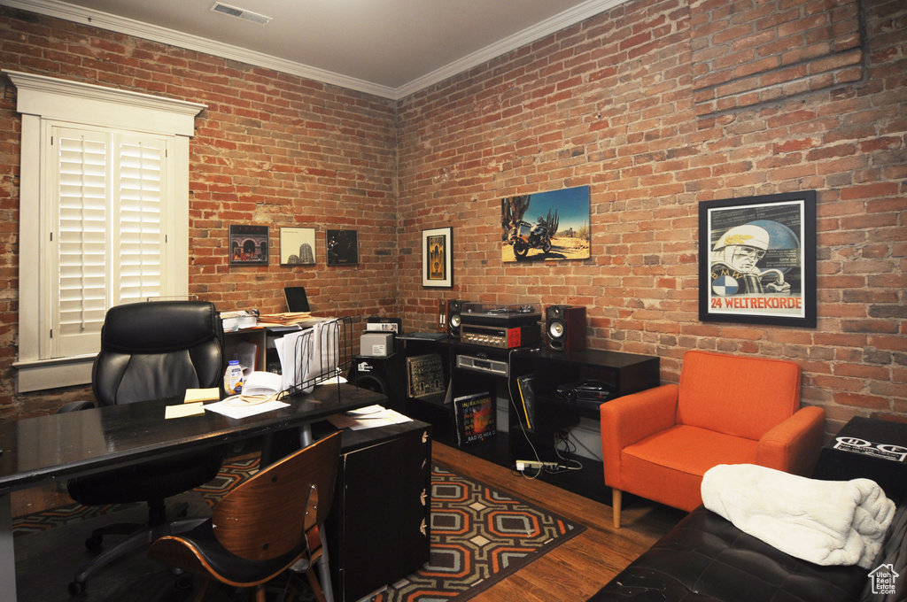 Office area with dark hardwood / wood-style floors, crown molding, and brick wall