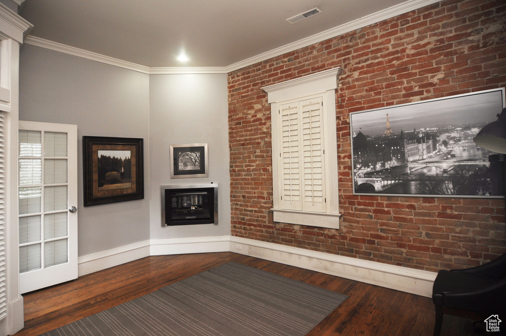 Interior space with crown molding, brick wall, and dark wood-type flooring
