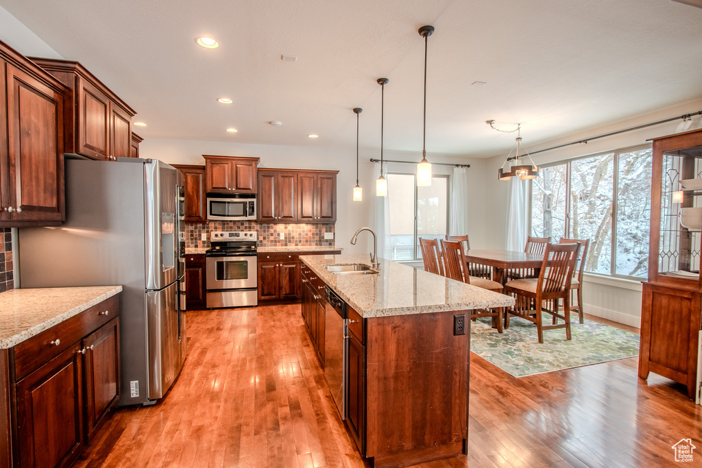 Kitchen featuring a kitchen island with sink, appliances with stainless steel finishes, light hardwood / wood-style flooring, and light stone countertops