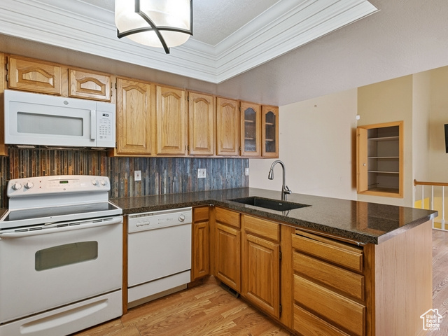 Kitchen with kitchen peninsula, white appliances, light hardwood / wood-style floors, sink, and ornamental molding