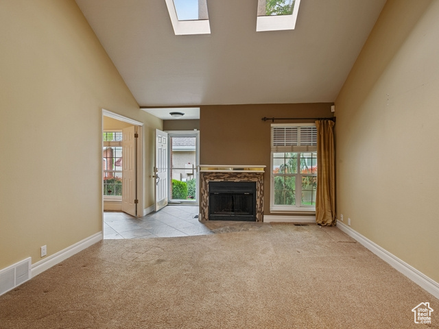 Unfurnished living room featuring light carpet, vaulted ceiling with skylight, and a healthy amount of sunlight