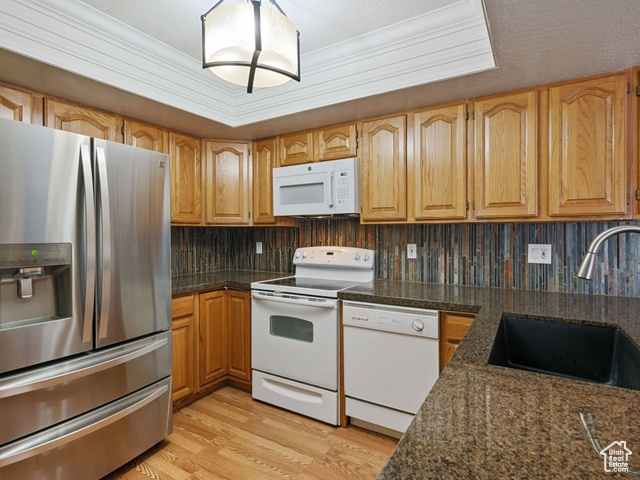 Kitchen with sink, white appliances, tasteful backsplash, light wood-type flooring, and dark stone countertops