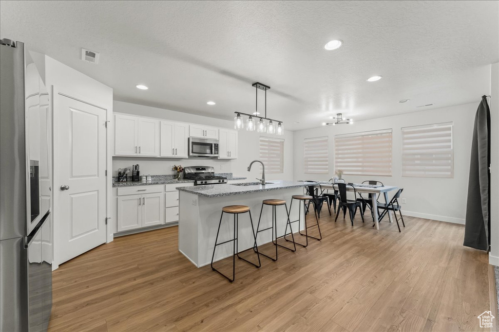Kitchen with decorative light fixtures, a center island with sink, light hardwood / wood-style floors, white cabinetry, and stainless steel appliances