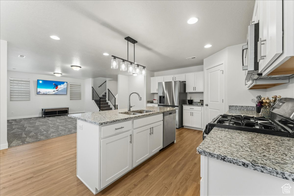 Kitchen featuring a kitchen island with sink, white cabinets, pendant lighting, light hardwood / wood-style floors, and appliances with stainless steel finishes