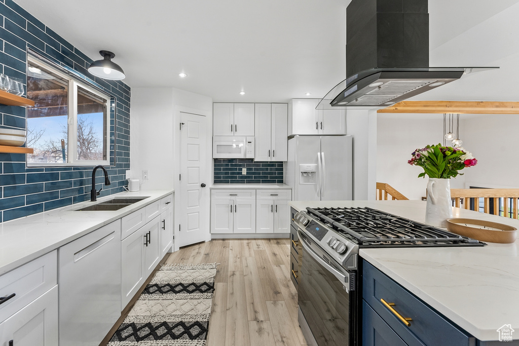 Kitchen with white appliances, island exhaust hood, backsplash, light hardwood / wood-style floors, and white cabinetry
