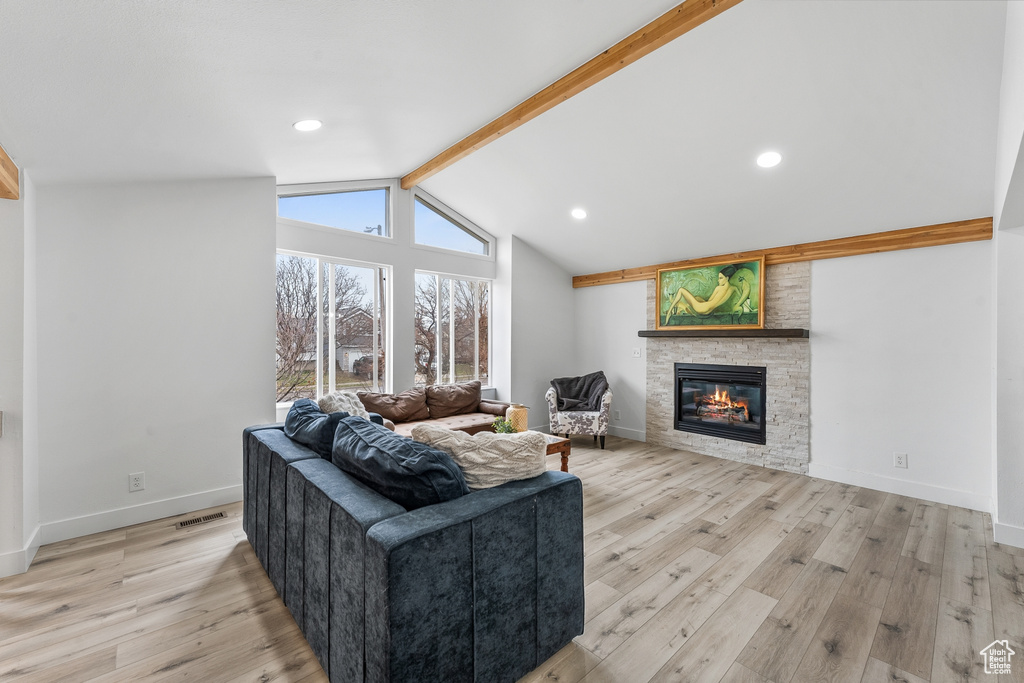 Living room featuring vaulted ceiling with beams, a stone fireplace, and light hardwood / wood-style floors