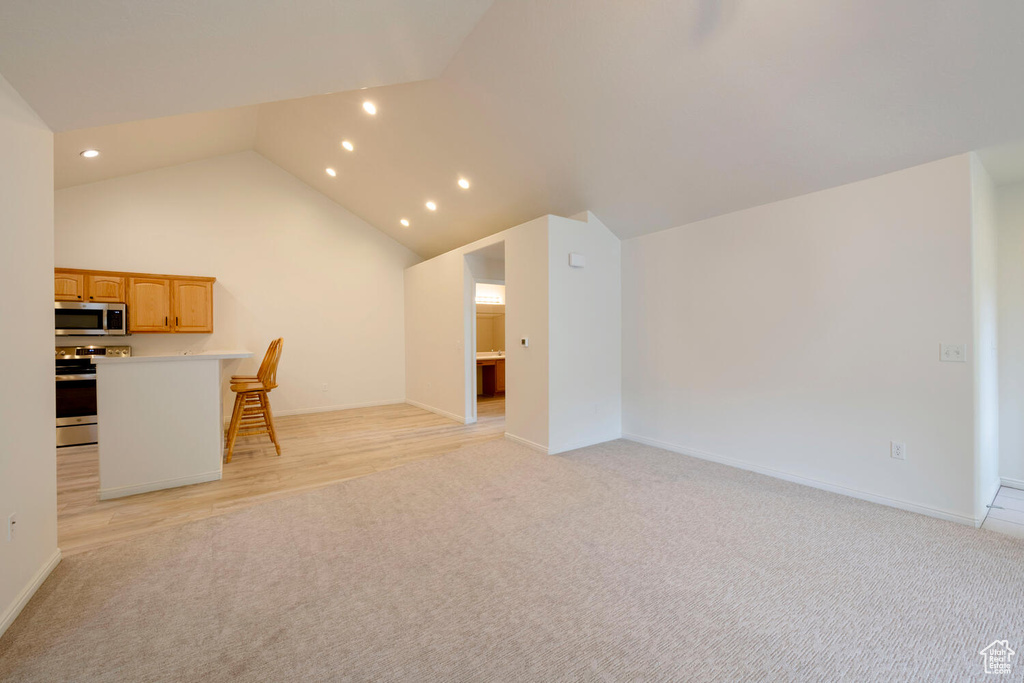 Unfurnished living room featuring light colored carpet and high vaulted ceiling