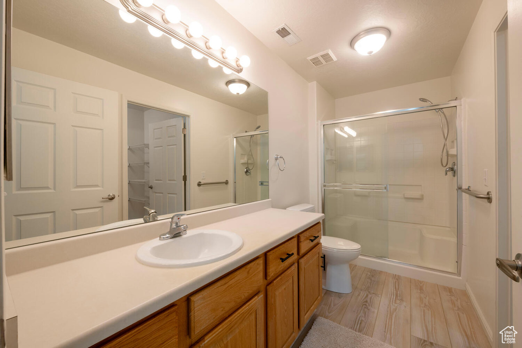 Bathroom featuring hardwood / wood-style floors, walk in shower, vanity with extensive cabinet space, and toilet