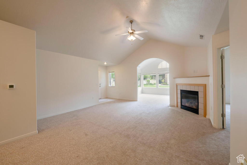 Unfurnished living room with light colored carpet, a tile fireplace, ceiling fan, and lofted ceiling